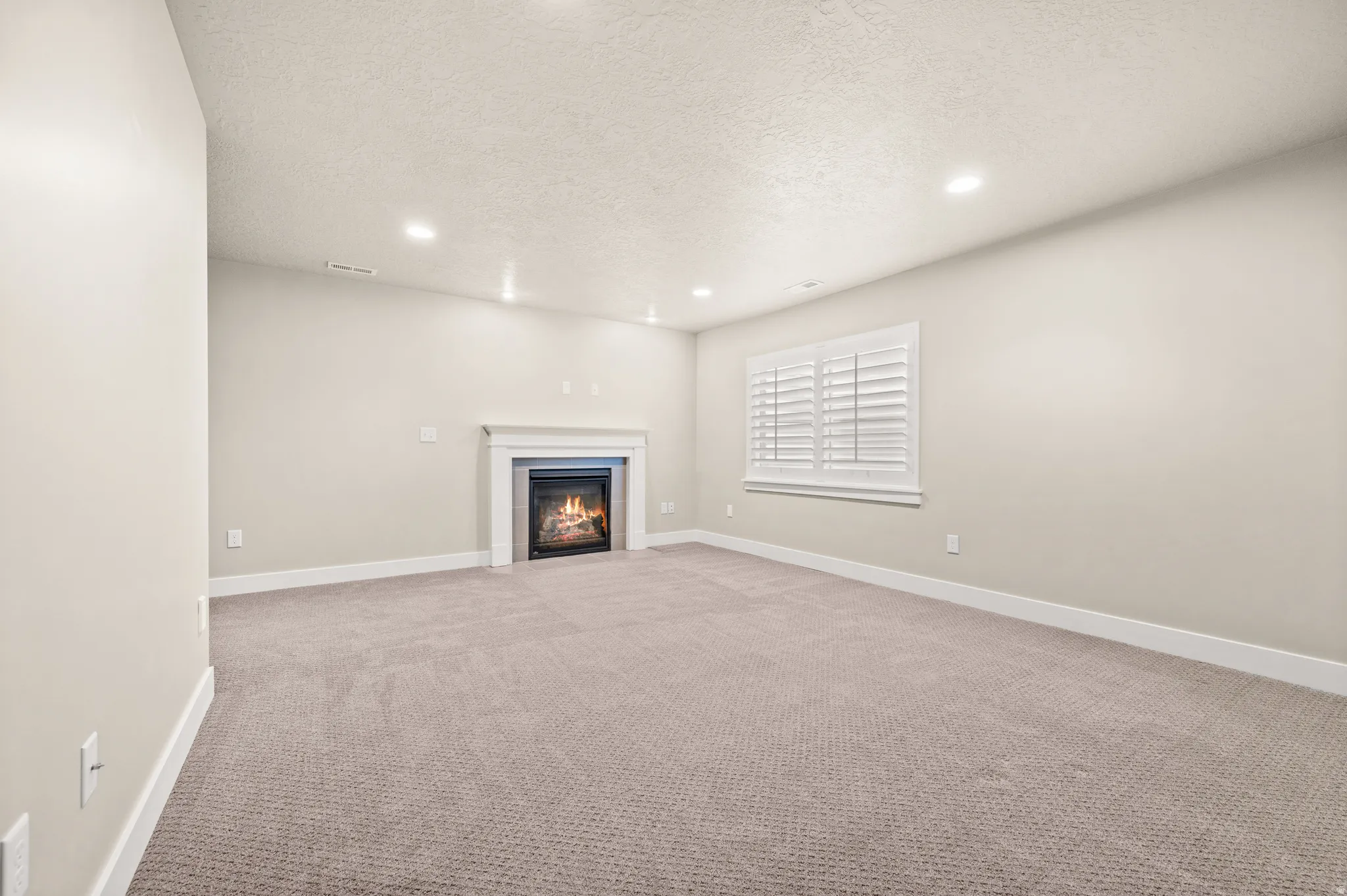 Spacious room featuring a central fireplace with a white mantel, recessed lighting, neutral wall paint, and plush carpeting