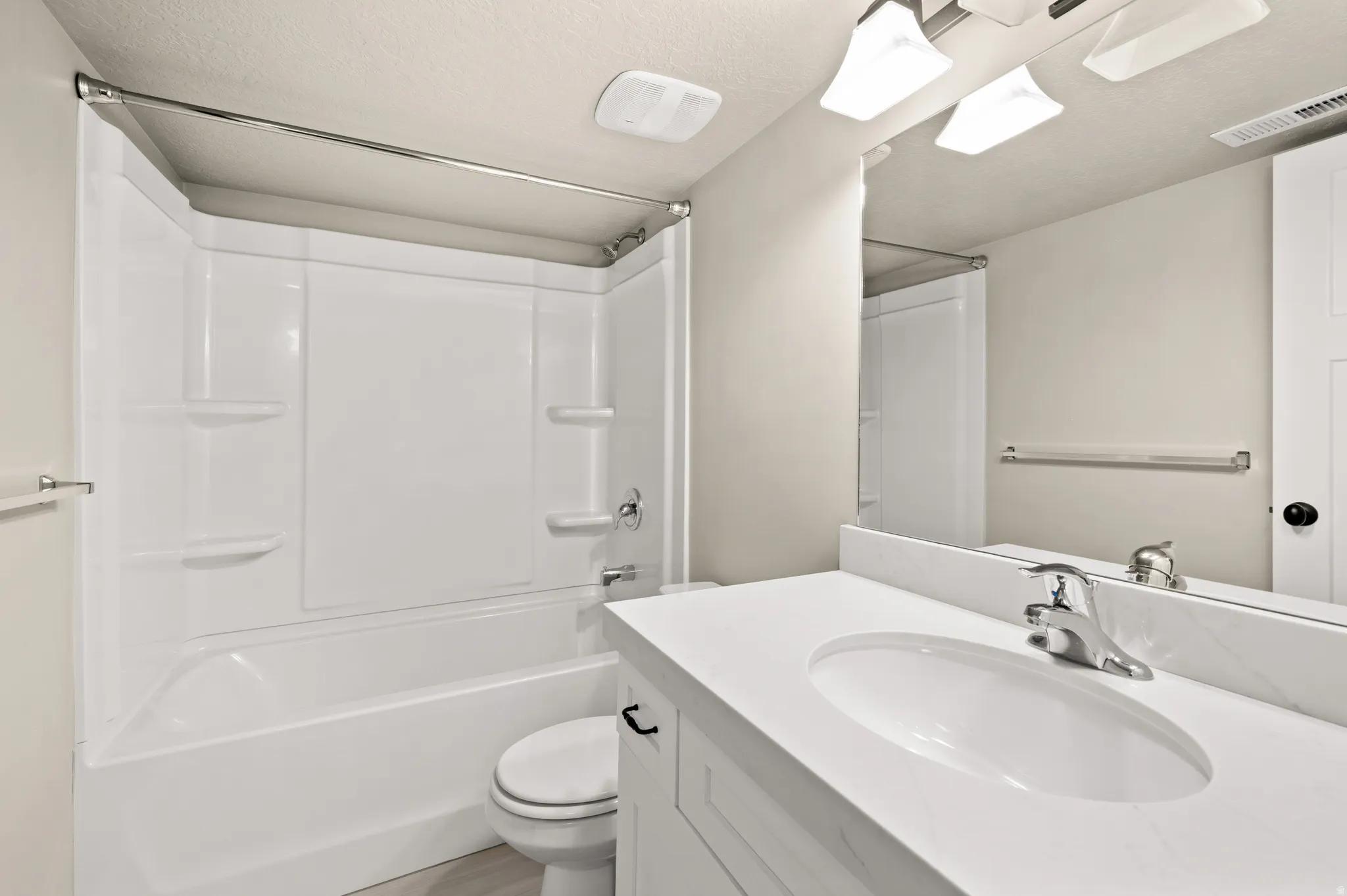 Bathroom featuring a white bathtub and shower surround, a white vanity with an integrated sink, a polished chrome faucet, and a large wall-mounted mirror
