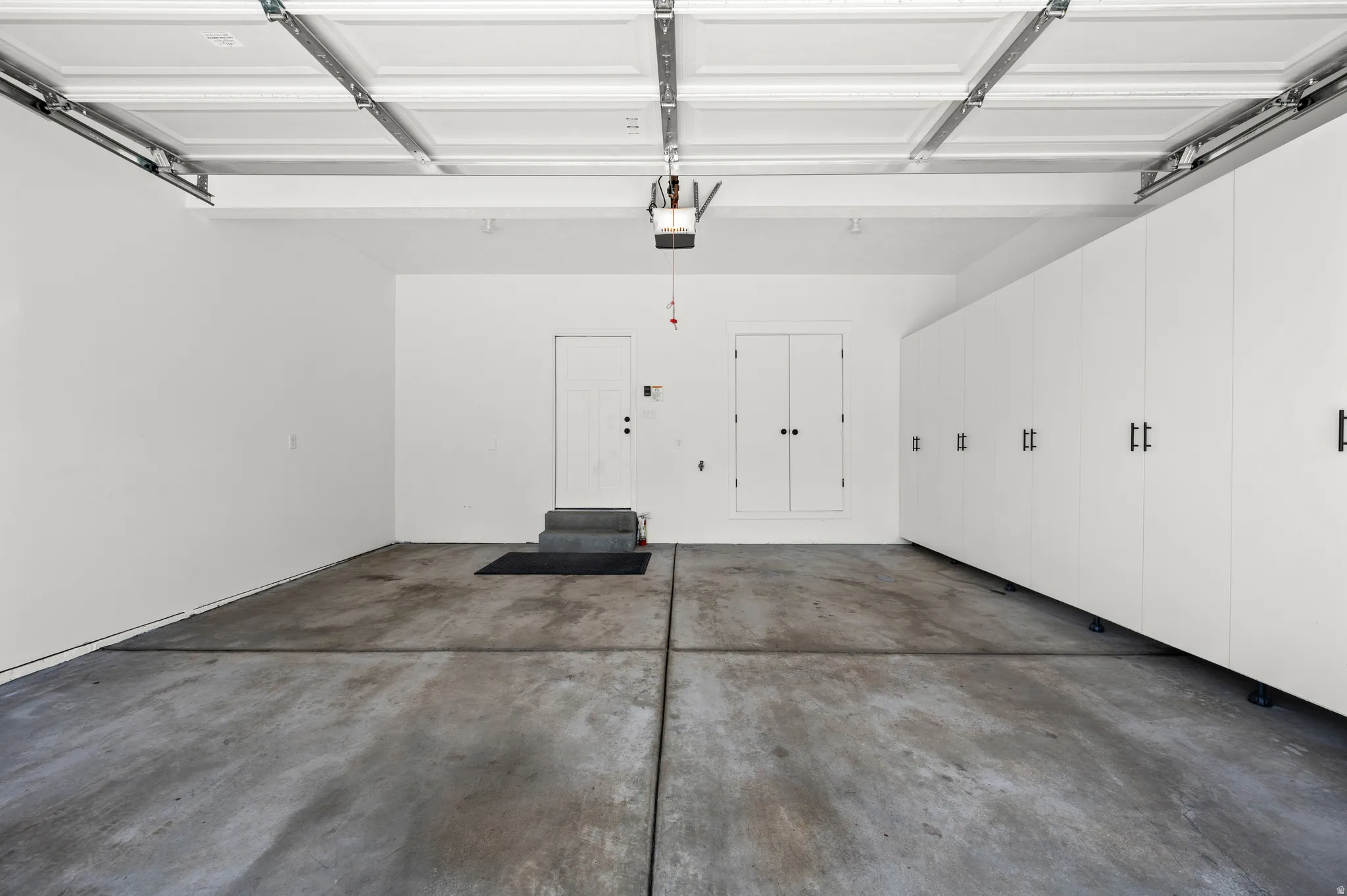 Spacious garage featuring a concrete floor, overhead door mechanism, and extensive built-in cabinetry with black hardware