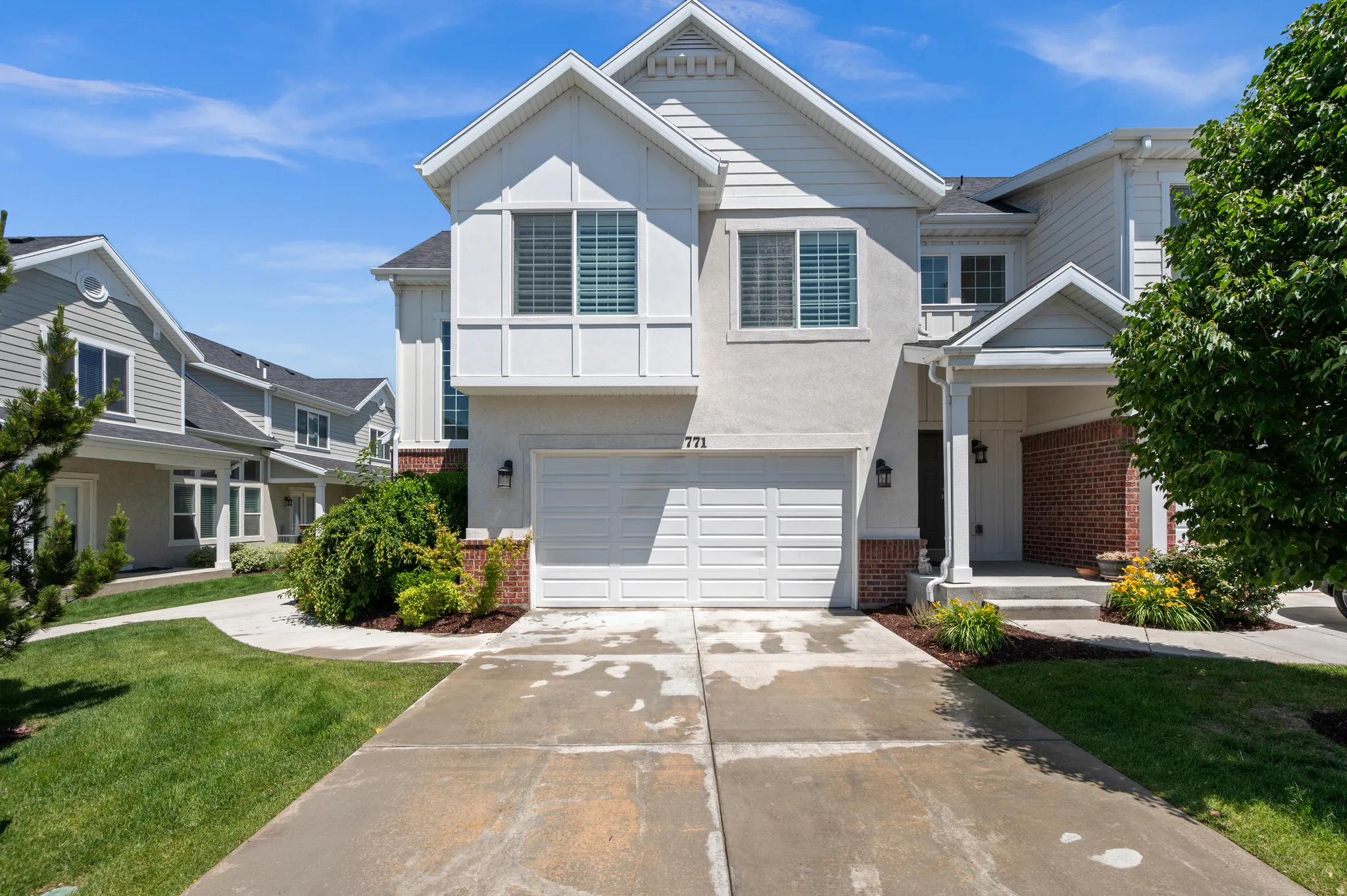 Contemporary townhouse exterior featuring a two-car garage, covered porch entry, white siding, and brick accents