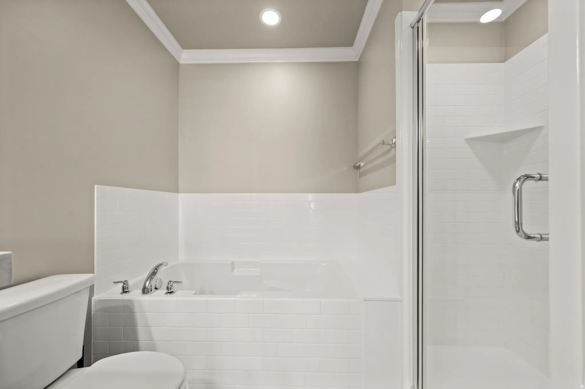 Built-in soaking tub with chrome fixtures, enclosed shower with glass door and built-in shelving, white subway tile surround, crown molding, and recessed lighting