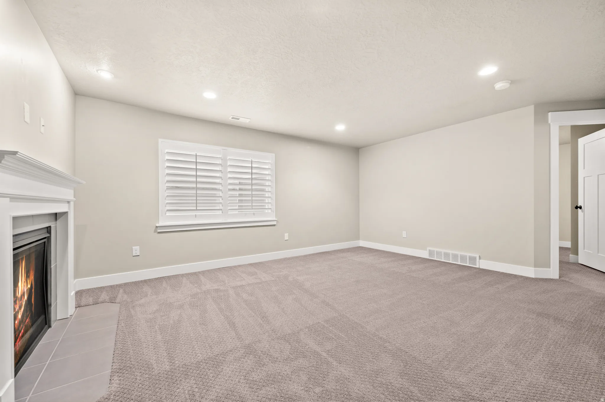 Carpeted room featuring a white-mantled fireplace with a tile hearth
