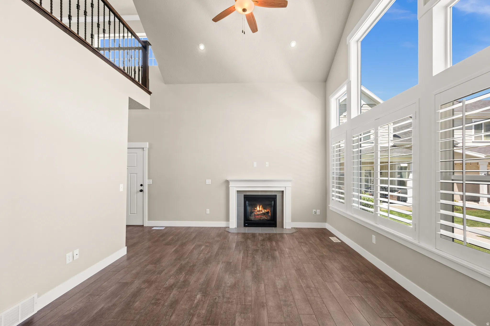 Spacious living area featuring high vaulted ceilings, wood-finish flooring, and a fireplace with a mantel