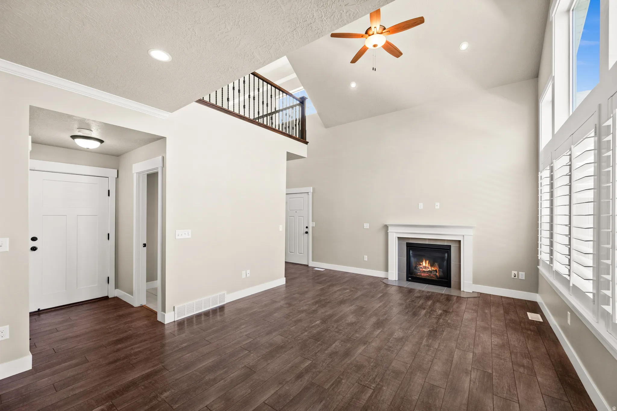 Vaulted living area featuring wood-finish flooring, a fireplace with a white mantel, and large windows with plantation shutters