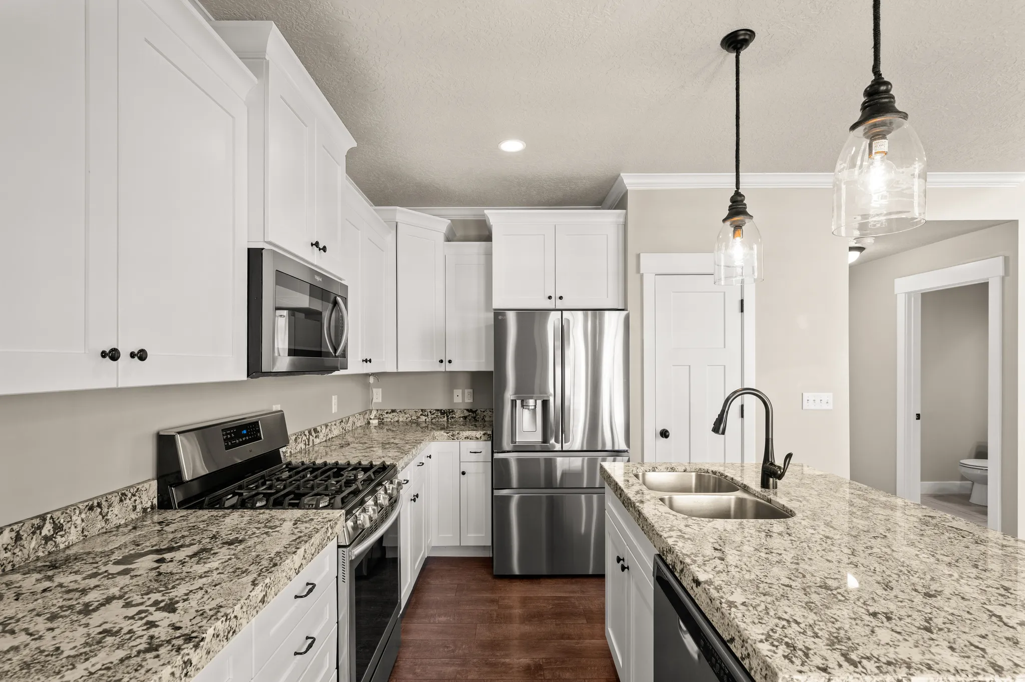 Kitchen featuring extensive light granite countertops, stainless steel appliances, white shaker cabinetry, wood-finish flooring, and pendant lighting