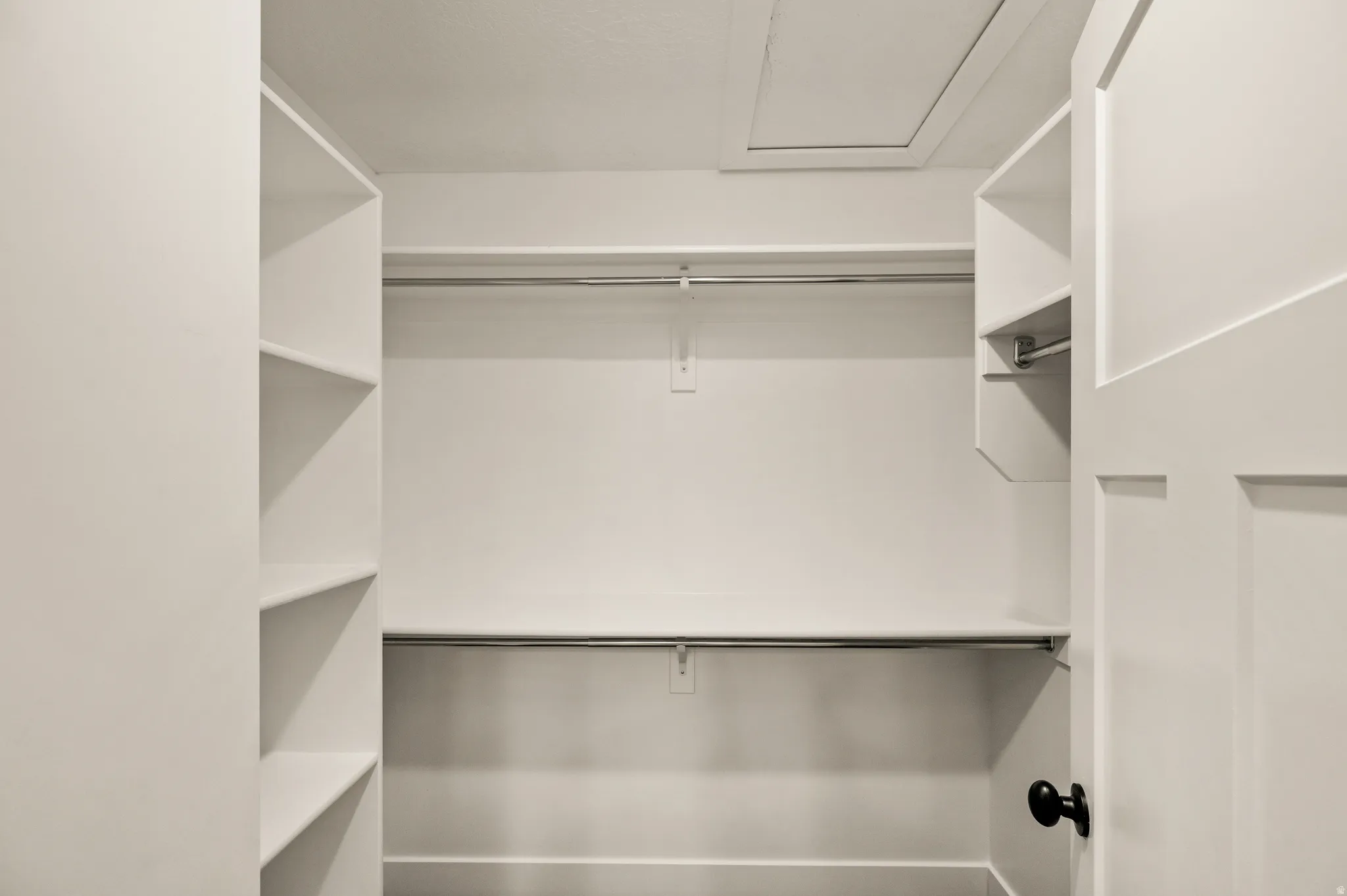 Walk-in closet featuring built-in shelving, two hanging rods, and an access panel