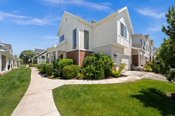 Townhome exterior featuring white vertical siding, brick accents, a gabled roofline, and an attached garage