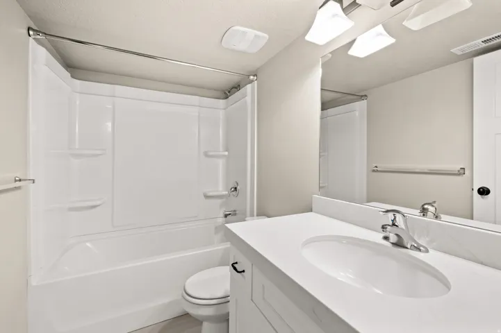 Bathroom featuring a white bathtub and shower surround, a white vanity with an integrated sink, a polished chrome faucet, and a large wall-mounted mirror