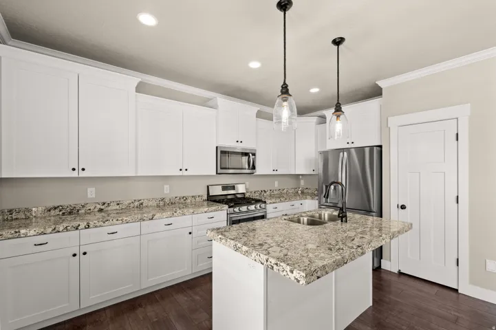 Modern kitchen featuring white cabinetry, stone countertops, stainless steel appliances, a center island with an undermount sink, and recessed lighting