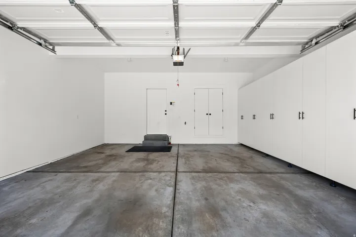 Spacious garage featuring a concrete floor, overhead door mechanism, and extensive built-in cabinetry with black hardware