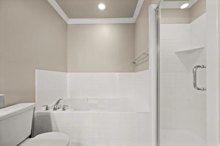 Built-in soaking tub with chrome fixtures, enclosed shower with glass door and built-in shelving, white subway tile surround, crown molding, and recessed lighting