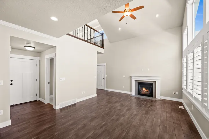 Vaulted living area featuring wood-finish flooring, a fireplace with a white mantel, and large windows with plantation shutters