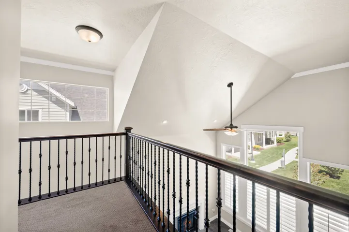 Open loft area featuring a wrought iron railing, vaulted ceilings, a ceiling fan, and multiple windows with plantation shutters