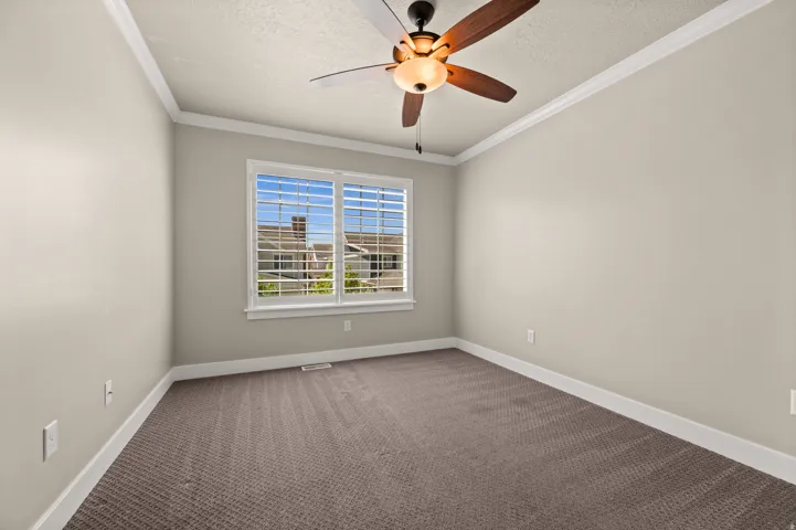 Bedroom featuring a ceiling fan with integrated lighting, crown molding, and neutral-toned carpeting