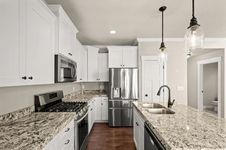 Kitchen featuring extensive light granite countertops, stainless steel appliances, white shaker cabinetry, wood-finish flooring, and pendant lighting