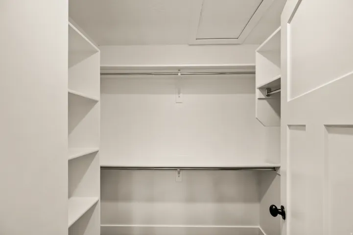 Walk-in closet featuring built-in shelving, two hanging rods, and an access panel