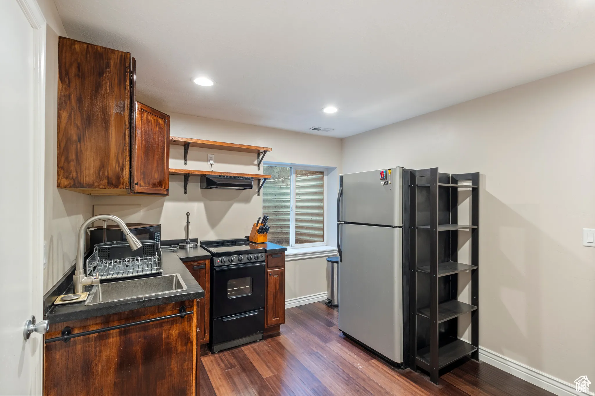 Kitchenette featuring wood-finish flooring, dark wood cabinetry, a stainless steel sink, and an electric range