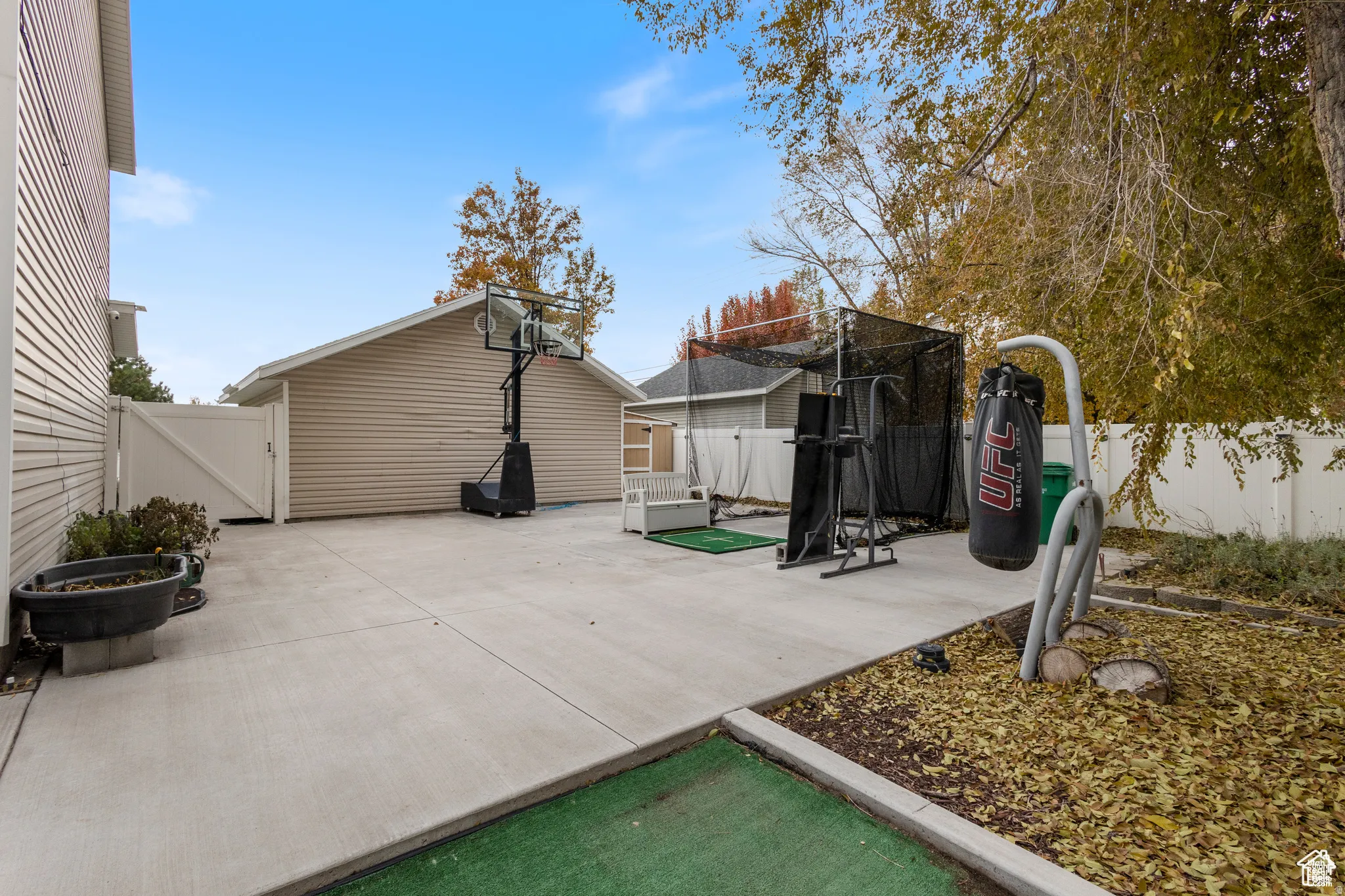 Concrete patio space featuring a privacy fence, detached garage, and mature trees