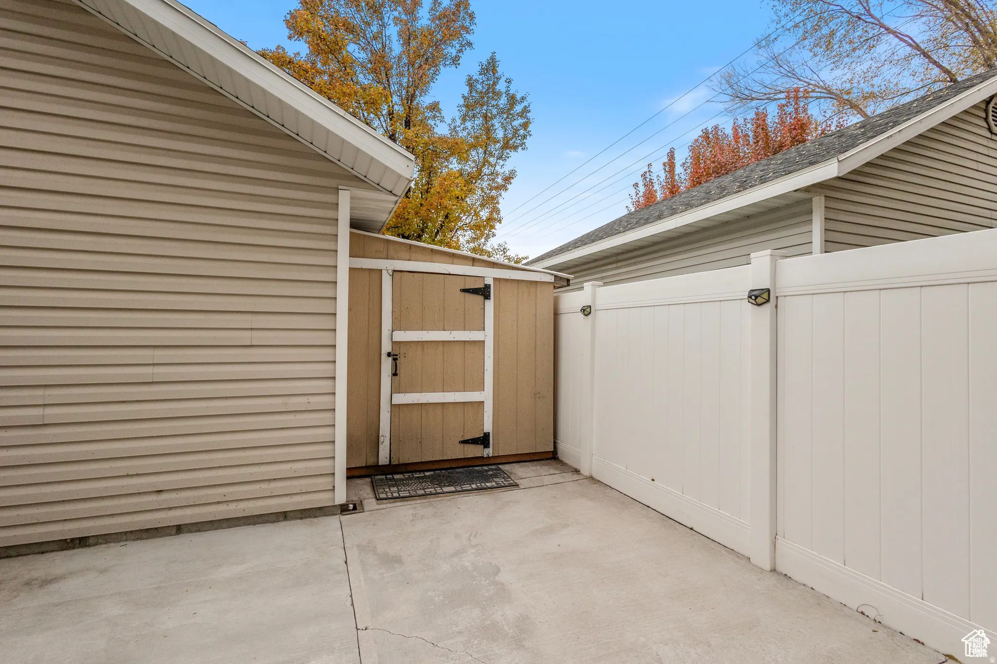 Concrete patio area featuring a storage shed with a paneled door, black hardware, and an opaque privacy fence