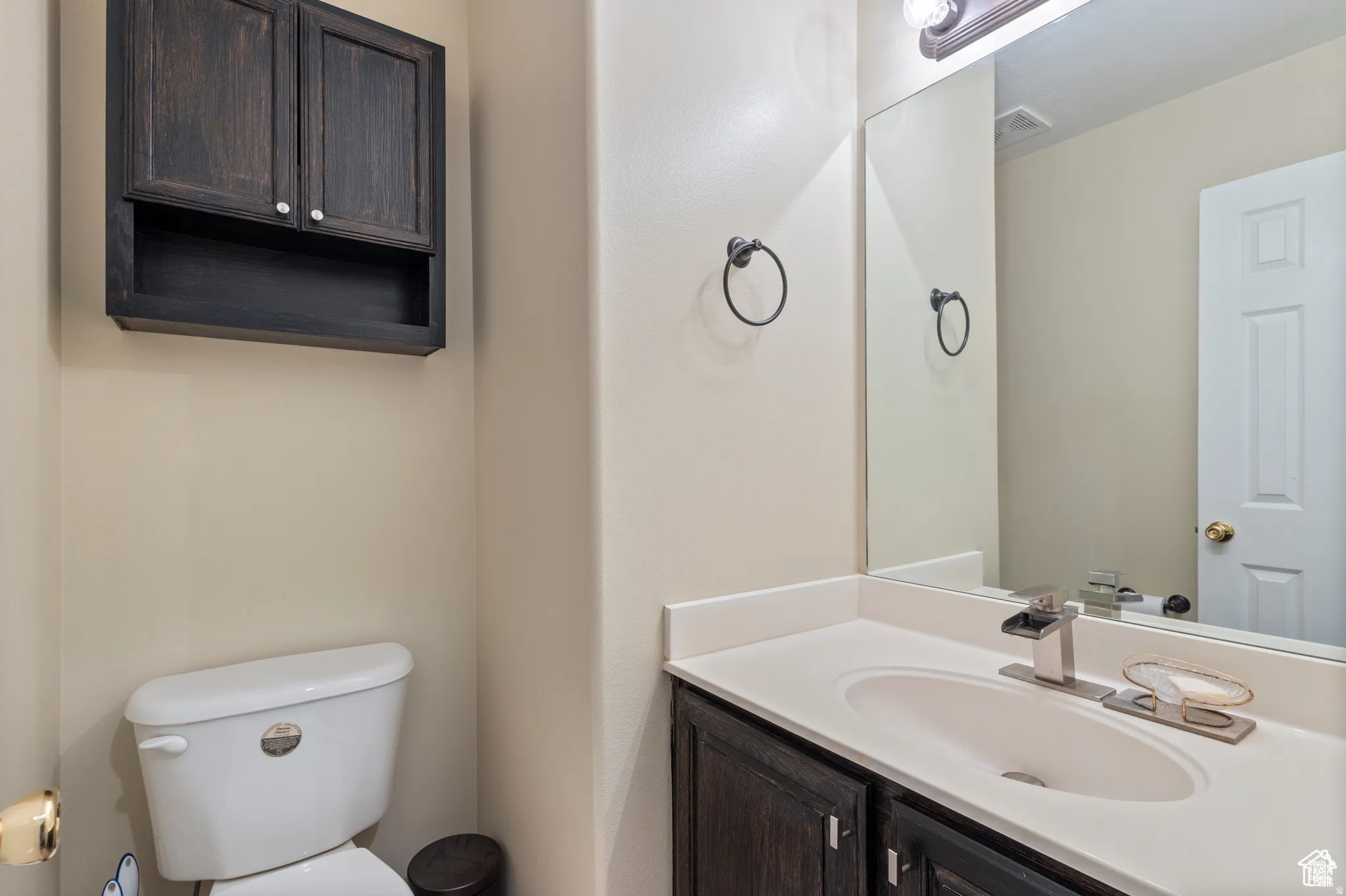 Bathroom featuring a dark wood-finish vanity with an integrated sink, polished chrome faucet, and a large wall-mounted mirror