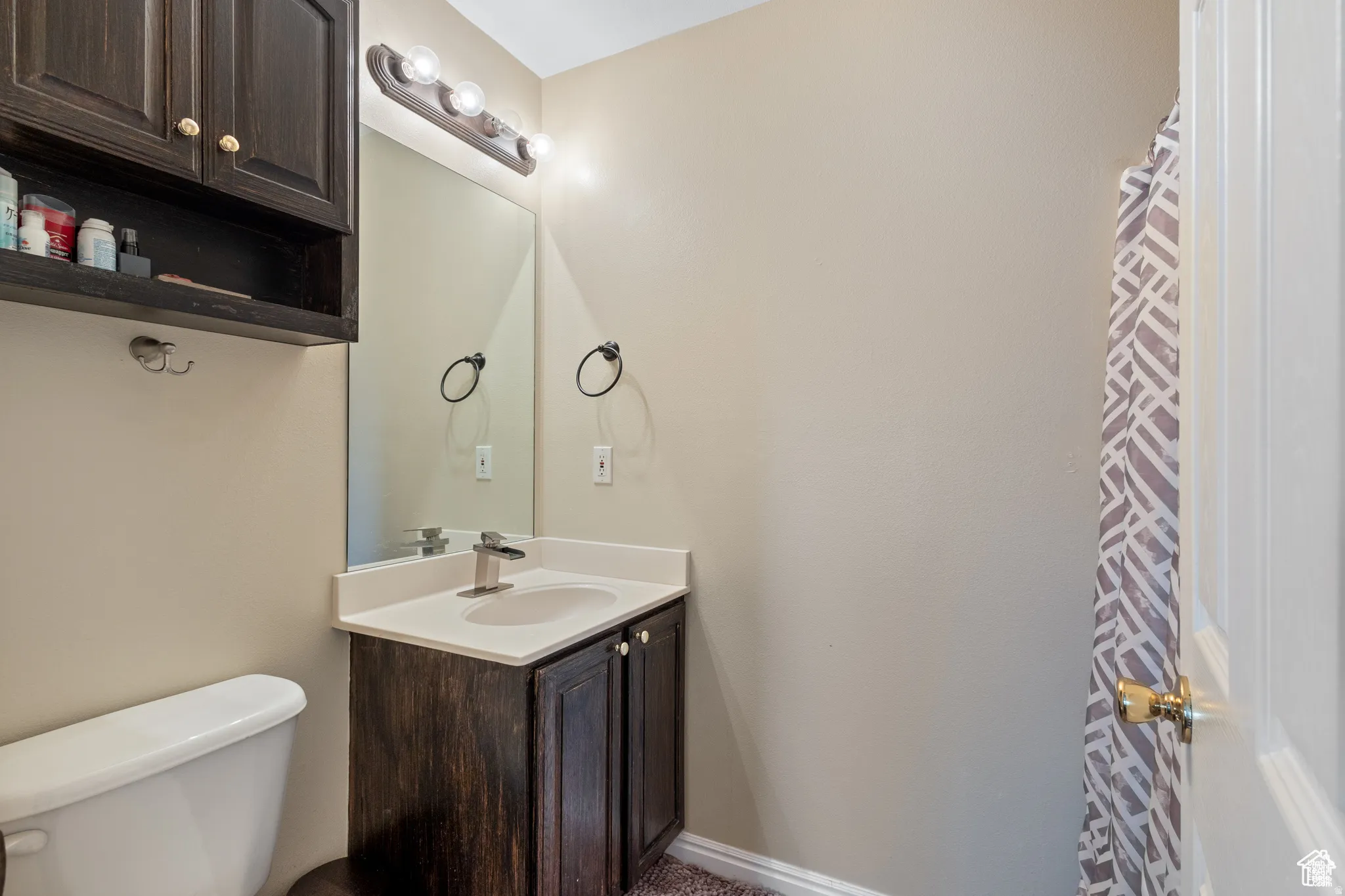 Bathroom featuring a dark wood-finish vanity with an integrated sink, a large wall mirror, and a three-bulb vanity light fixture
