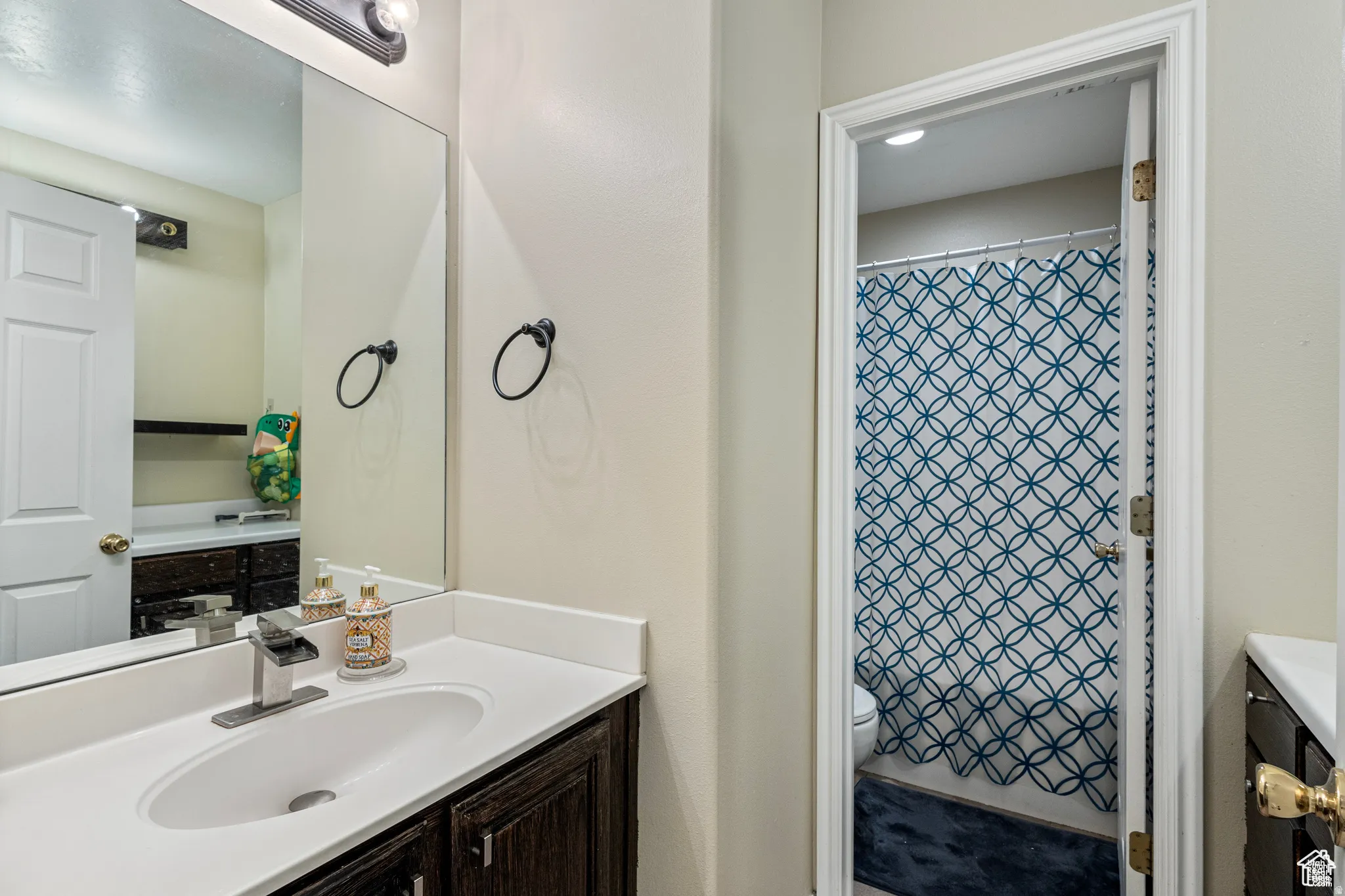 Bathroom featuring a single vanity with a white countertop, an undermount sink, and dark wood-finish cabinetry