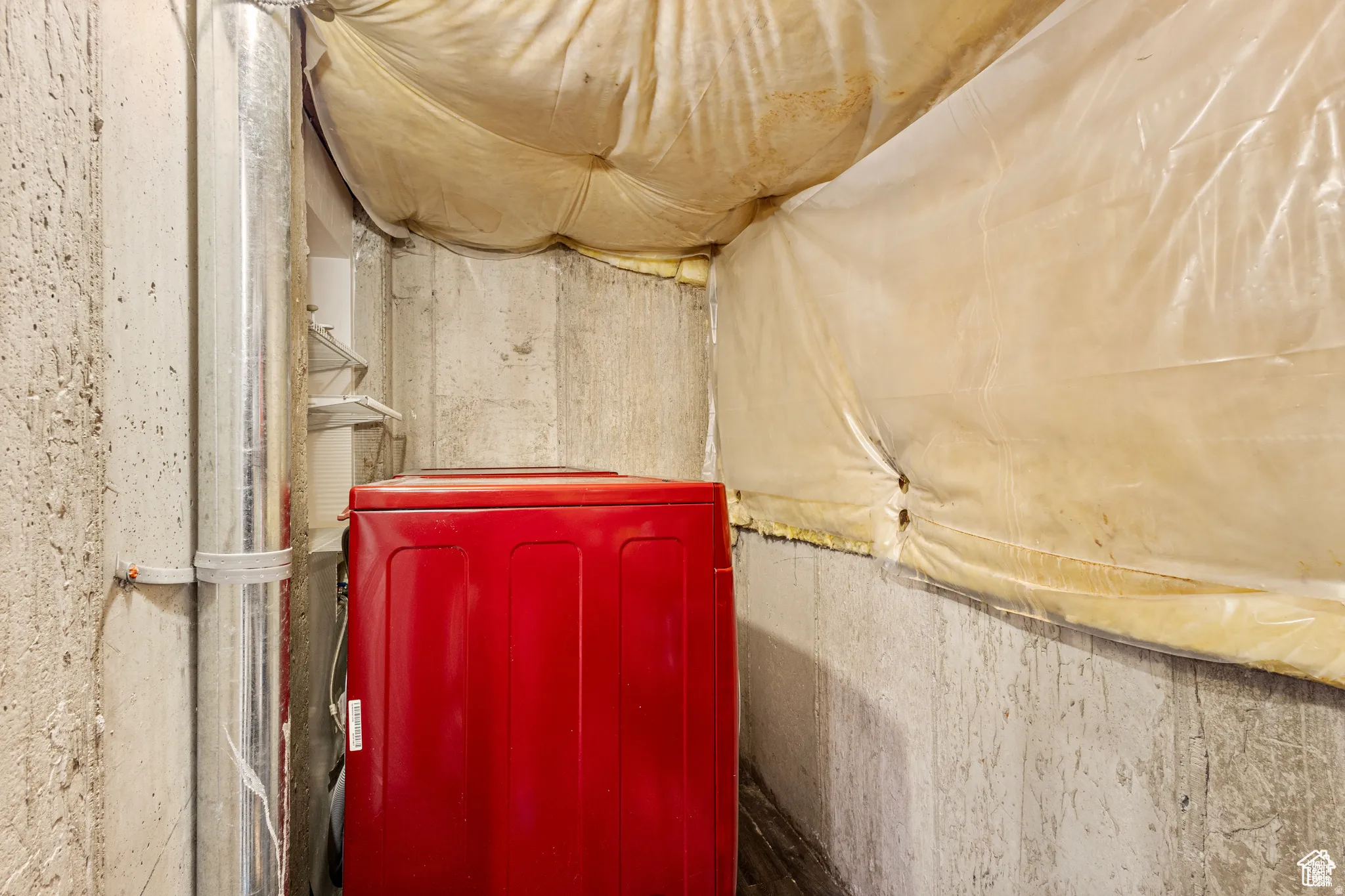 Concrete walls featuring a metal duct, visible insulation, and a red appliance
