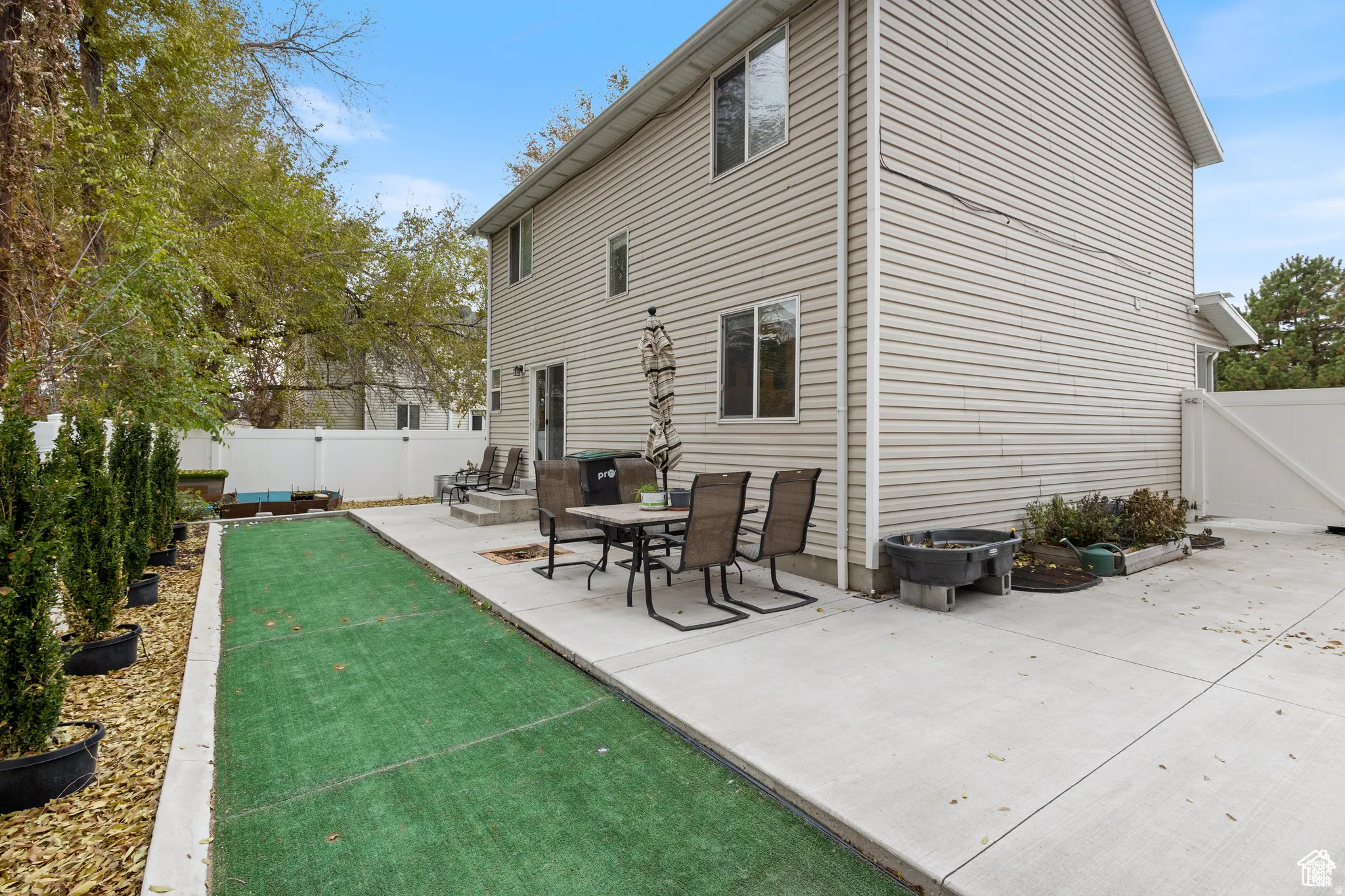 Rear exterior featuring a concrete patio, a strip of artificial turf, and a white vinyl privacy fence