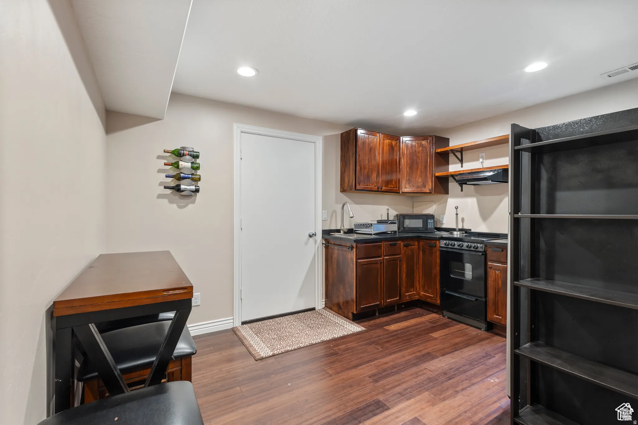 Compact kitchen area featuring wood-finish flooring, dark wood cabinetry, and a black countertop
