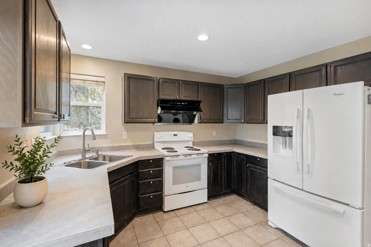 Kitchen featuring dark wood-finish cabinetry, light-toned countertops, a dual-basin stainless steel sink, and tile flooring