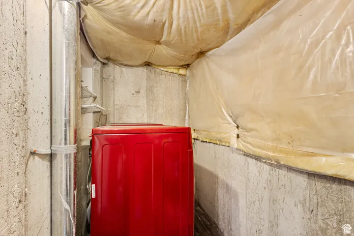 Concrete walls featuring a metal duct, visible insulation, and a red appliance