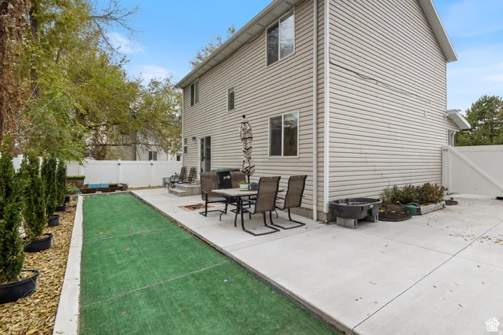 Rear exterior featuring a concrete patio, a strip of artificial turf, and a white vinyl privacy fence