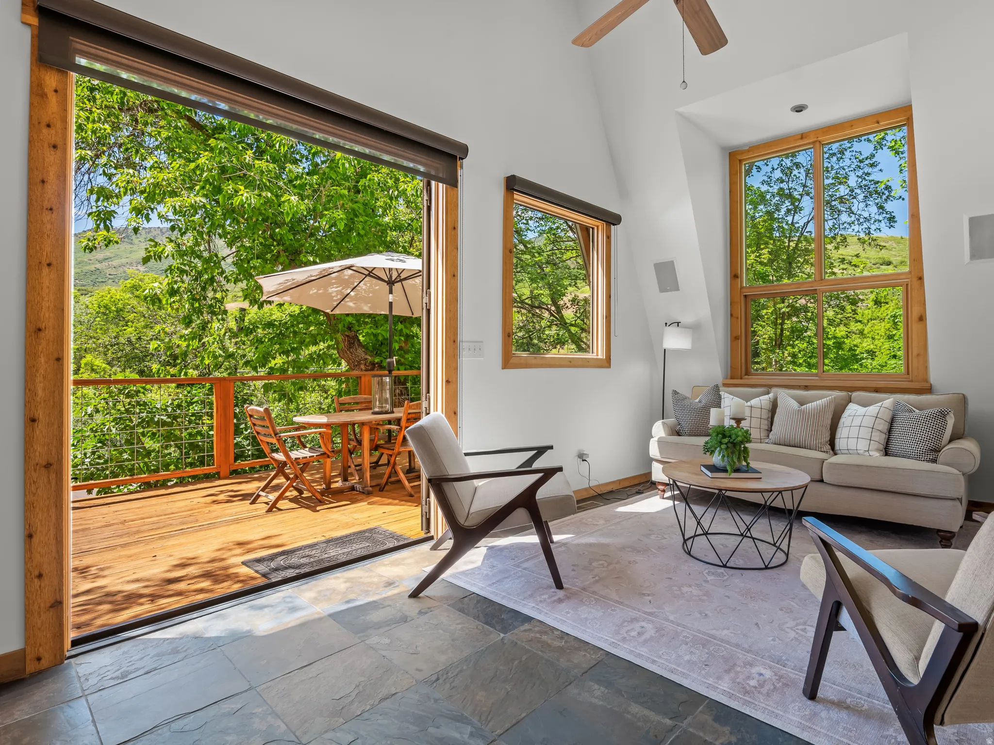 Spacious room featuring natural wood-trimmed French doors opening to a wood-plank deck, slate tile flooring, and a vaulted ceiling with a ceiling fan