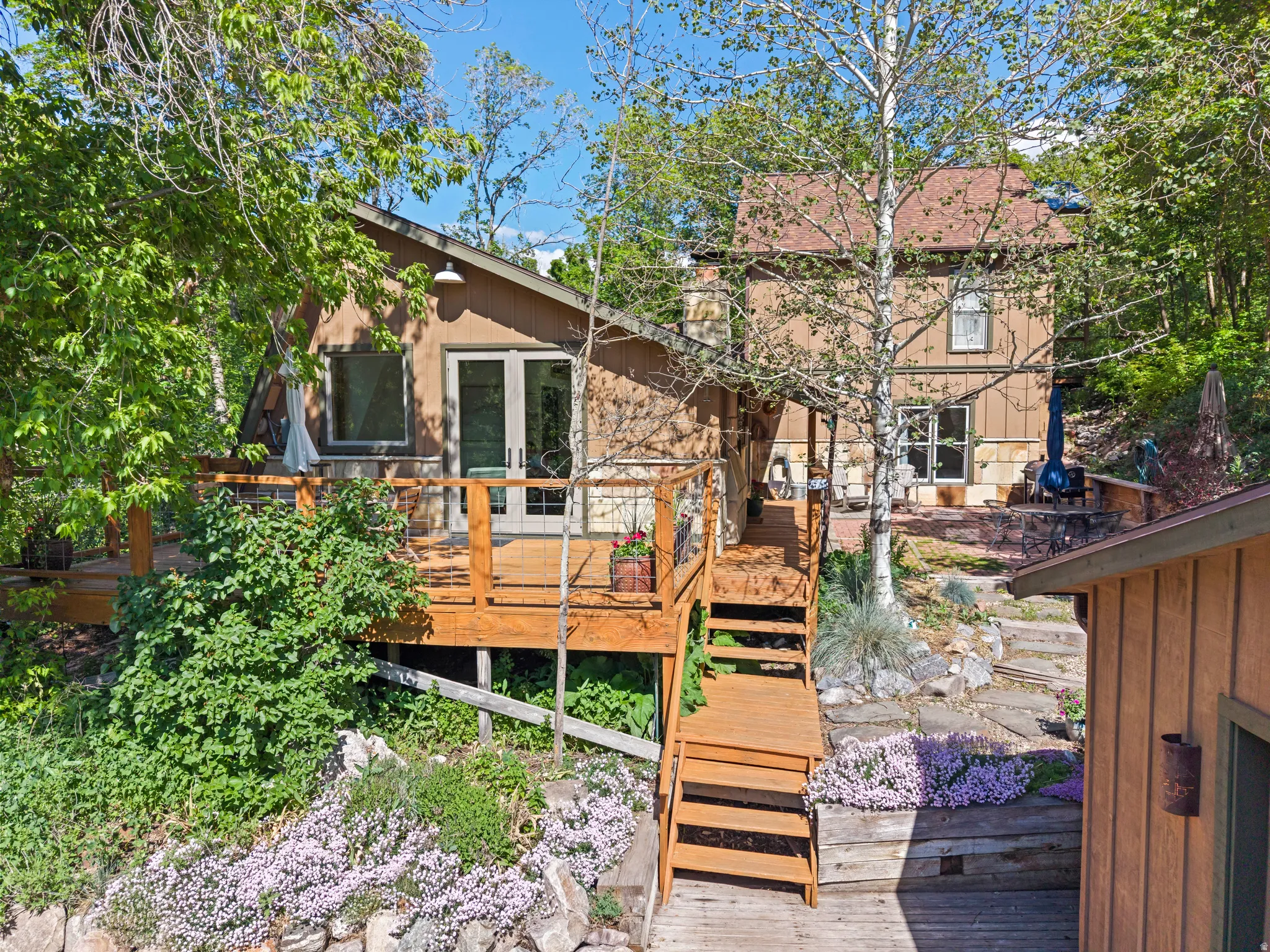 Multi-level deck and stairs with wooden railing, surrounded by mature trees and lush ground cover