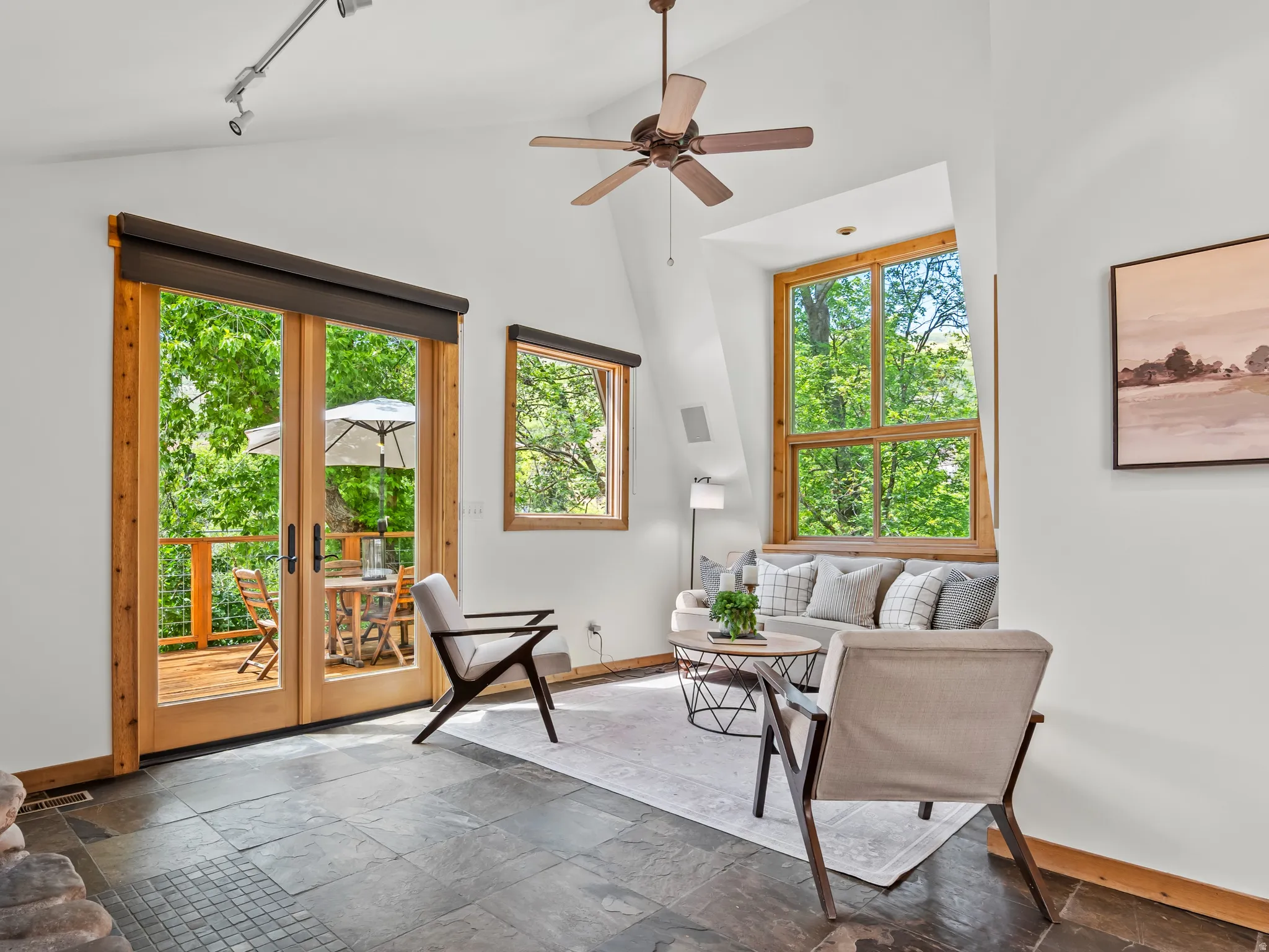 Living area featuring slate tile flooring, a stone fireplace, and a vaulted ceiling with a fan
