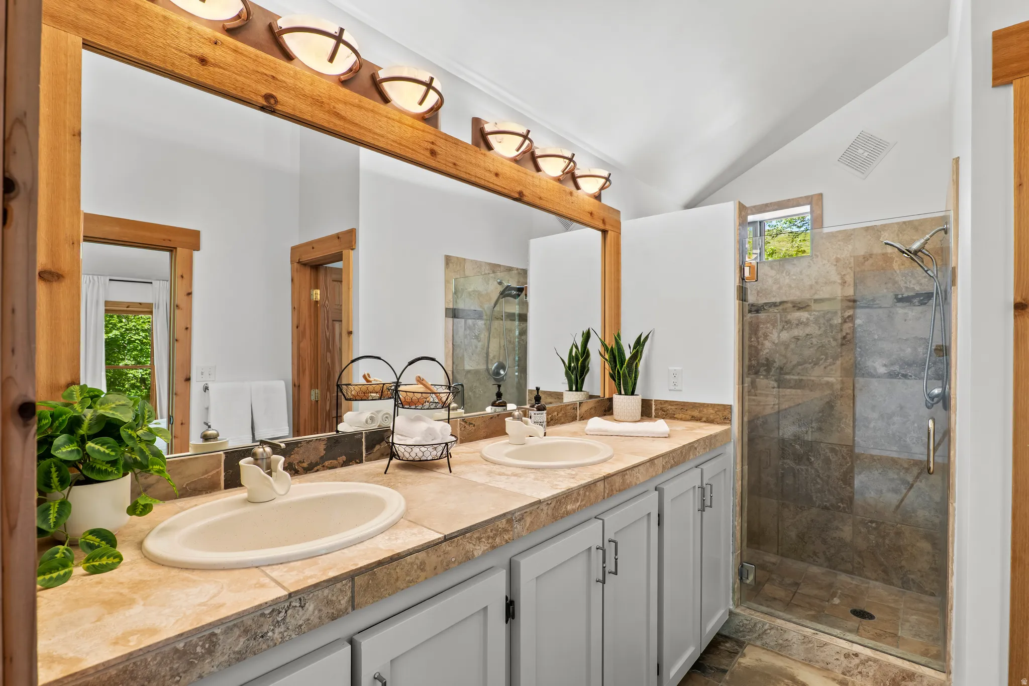 Double vanity with integrated sinks, stone-finish countertop, and light wood-framed mirror