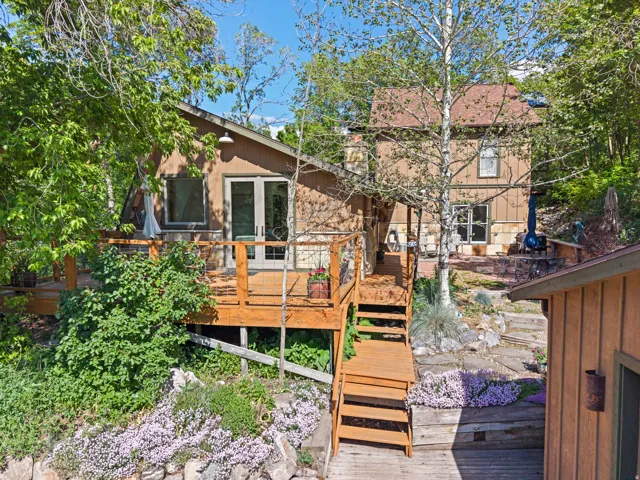 Multi-level deck and stairs with wooden railing, surrounded by mature trees and lush ground cover