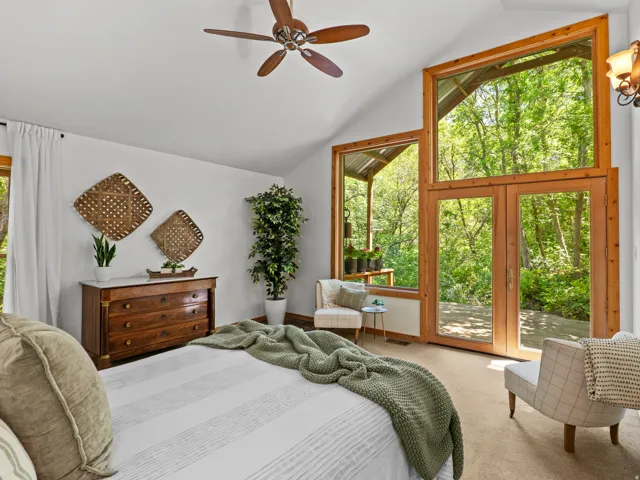 Vaulted ceilings with a ceiling fan, a large wooden framed window, a pair of wooden framed doors, and light-colored carpet flooring