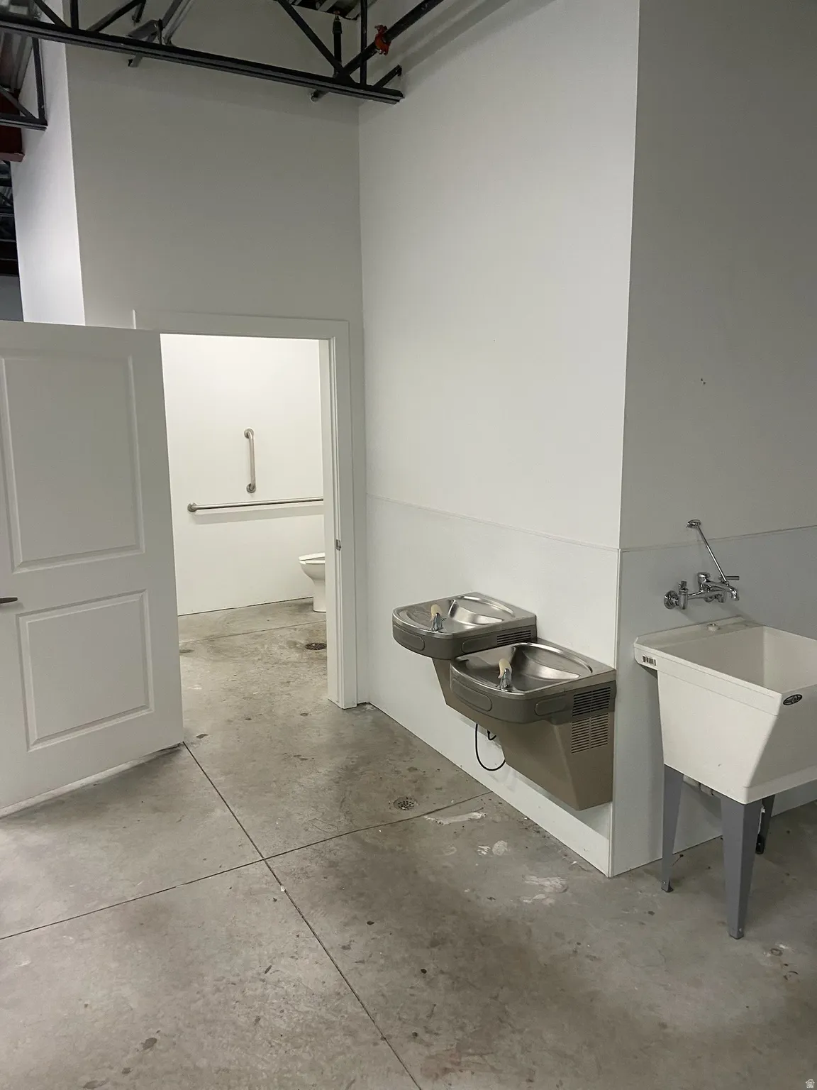 Utility area featuring two water fountains, a deep basin sink with wall-mounted faucets, and a concrete floor