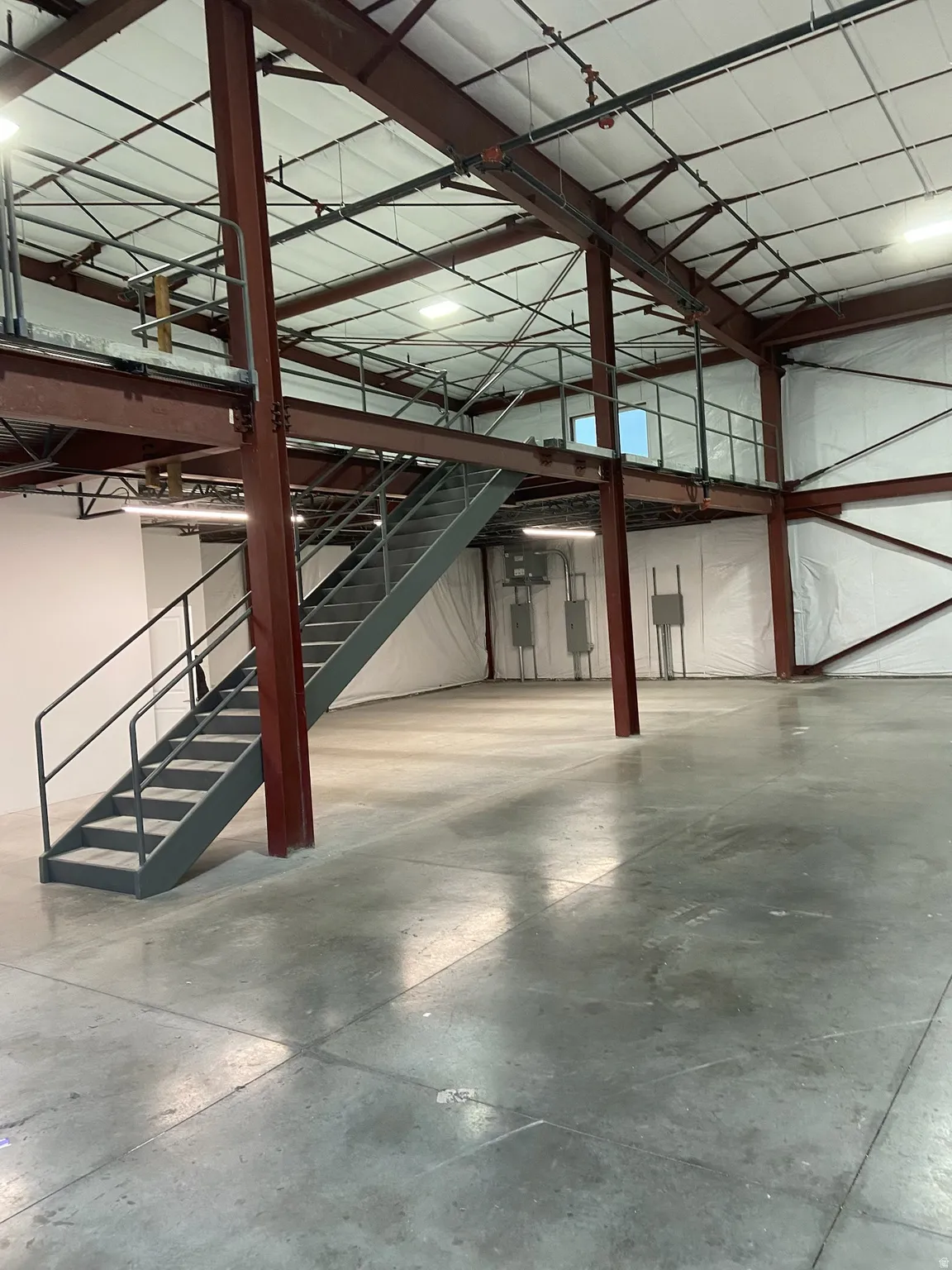 Expansive industrial interior featuring a mezzanine level with metal railings and staircase