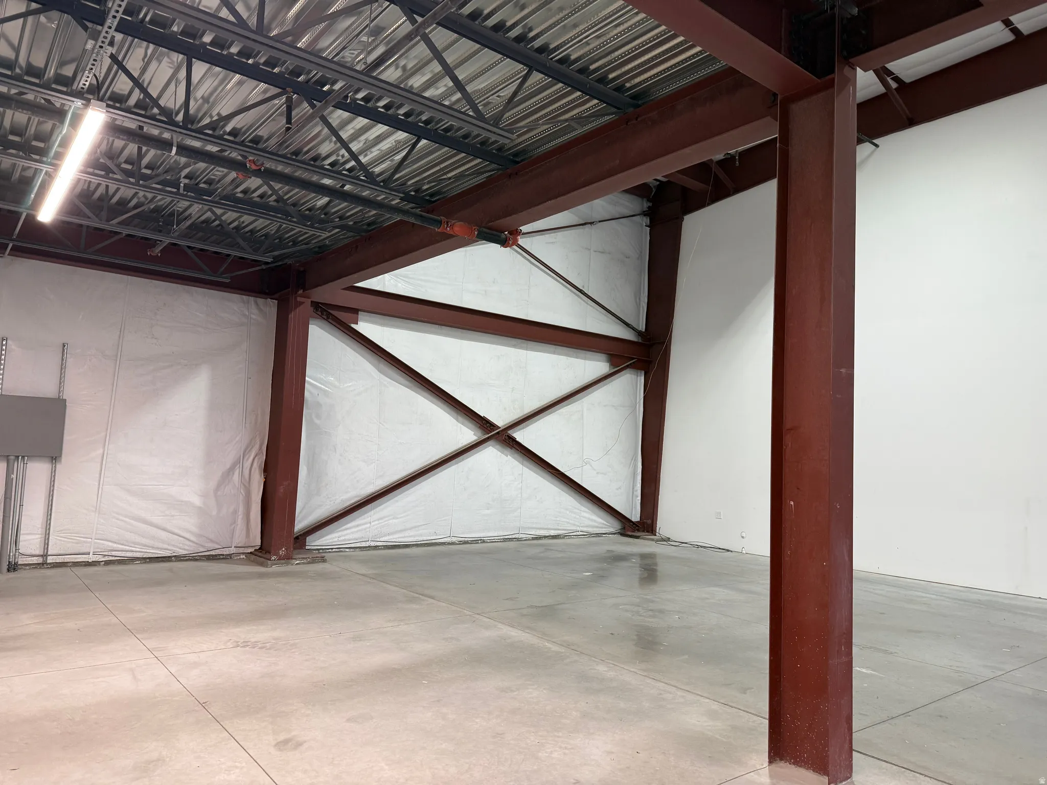 Industrial interior featuring exposed red structural steel beams and columns, a high metal deck ceiling with visible joists, concrete flooring, and white insulated wall panels