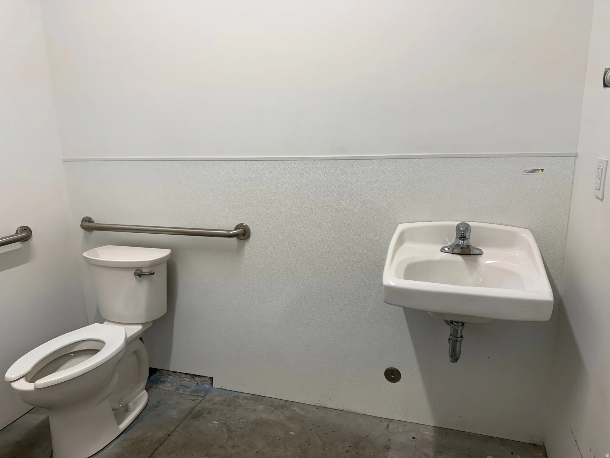 White wall-mounted sink with chrome faucet, complemented by a white toilet and stainless steel grab bars