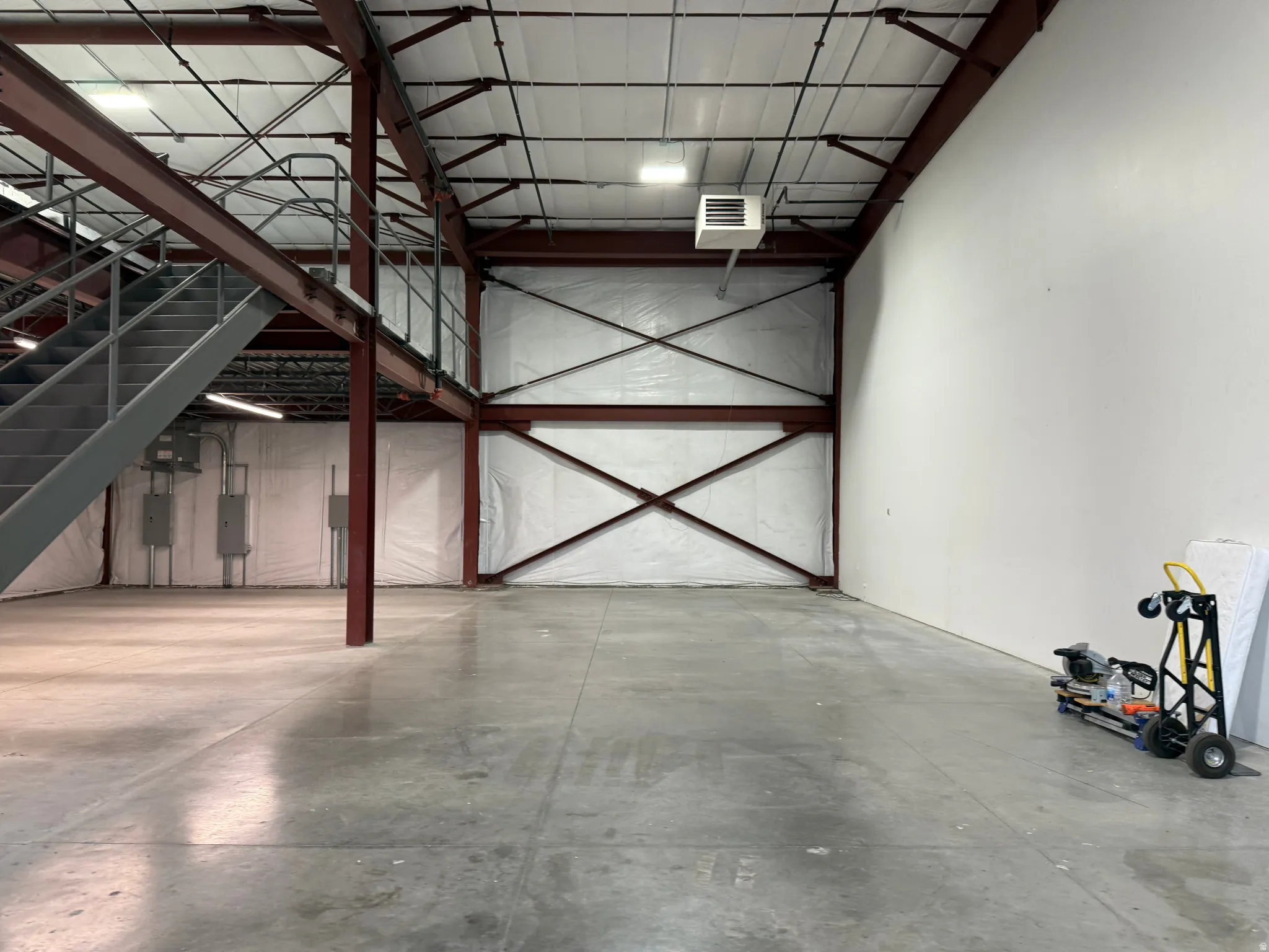 Spacious interior featuring a concrete floor, high ceilings with exposed metal beams, and a mezzanine level with a gray metal staircase