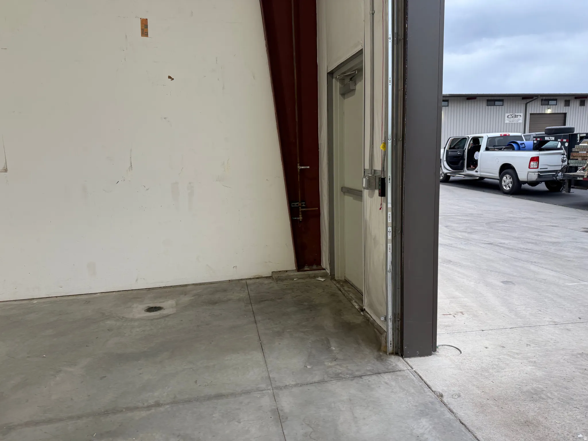 Concrete flooring with a floor drain, white finished walls, and an industrial-style metal door frame