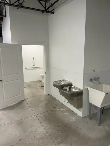 Utility area featuring two water fountains, a deep basin sink with wall-mounted faucets, and a concrete floor