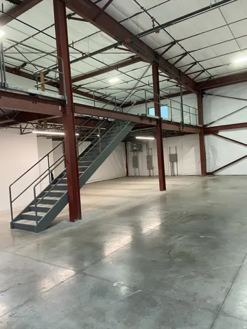 Expansive industrial interior featuring a mezzanine level with metal railings and staircase