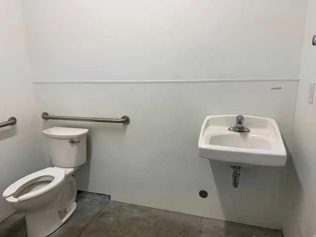 White wall-mounted sink with chrome faucet, complemented by a white toilet and stainless steel grab bars
