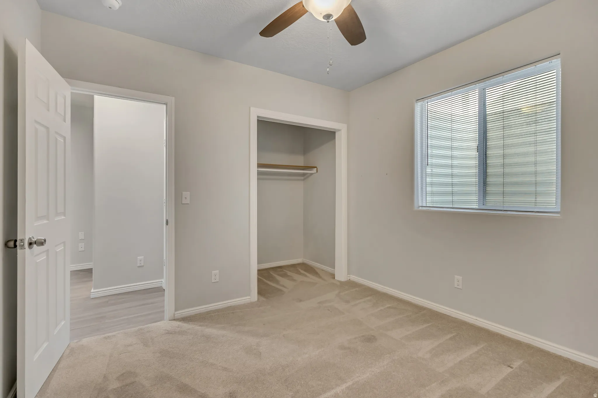 Neutral-toned carpeting and walls complement the ceiling fan with integrated lighting