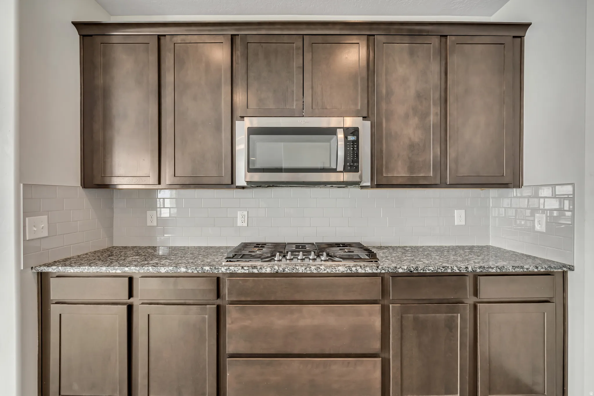 Kitchen featuring wood-finish cabinetry, stainless steel microwave, gas cooktop, granite countertops, and subway tile backsplash