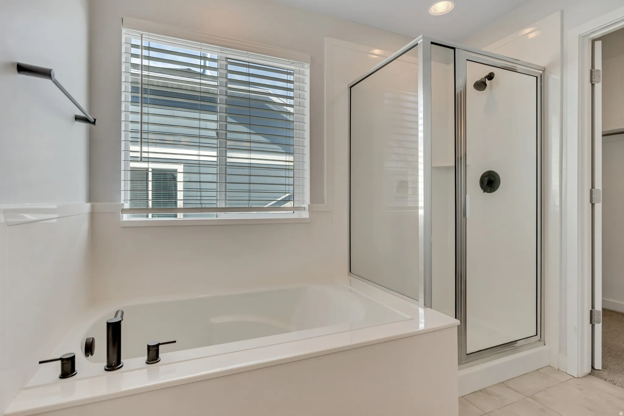 Contemporary bathroom featuring a built-in soaking tub with matte black fixtures, a separate shower enclosure with a glass door, recessed lighting, and a window with blinds
